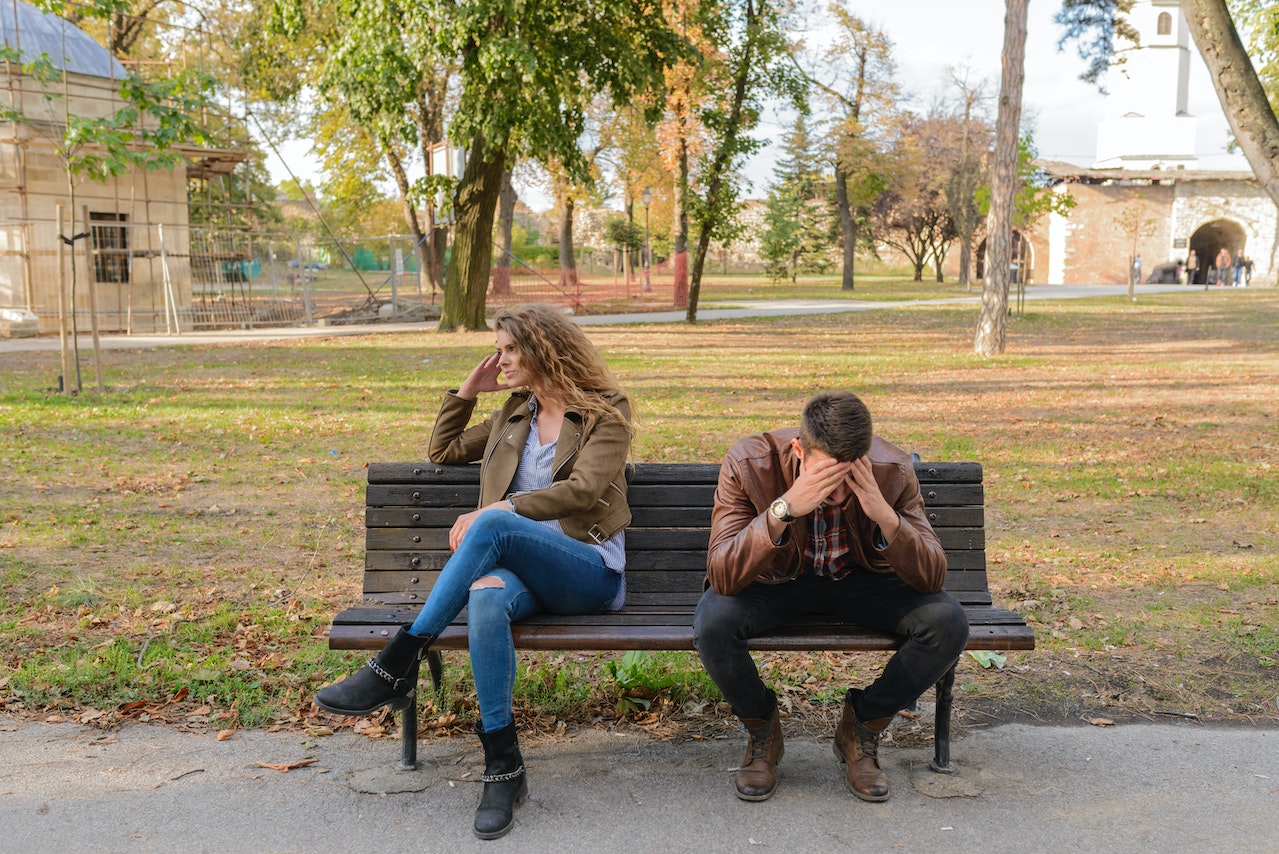 casal triste sentado em banco da praça devido ao bullying familiar